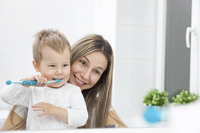 Criança escovando os dentes com ajuda da mãe
